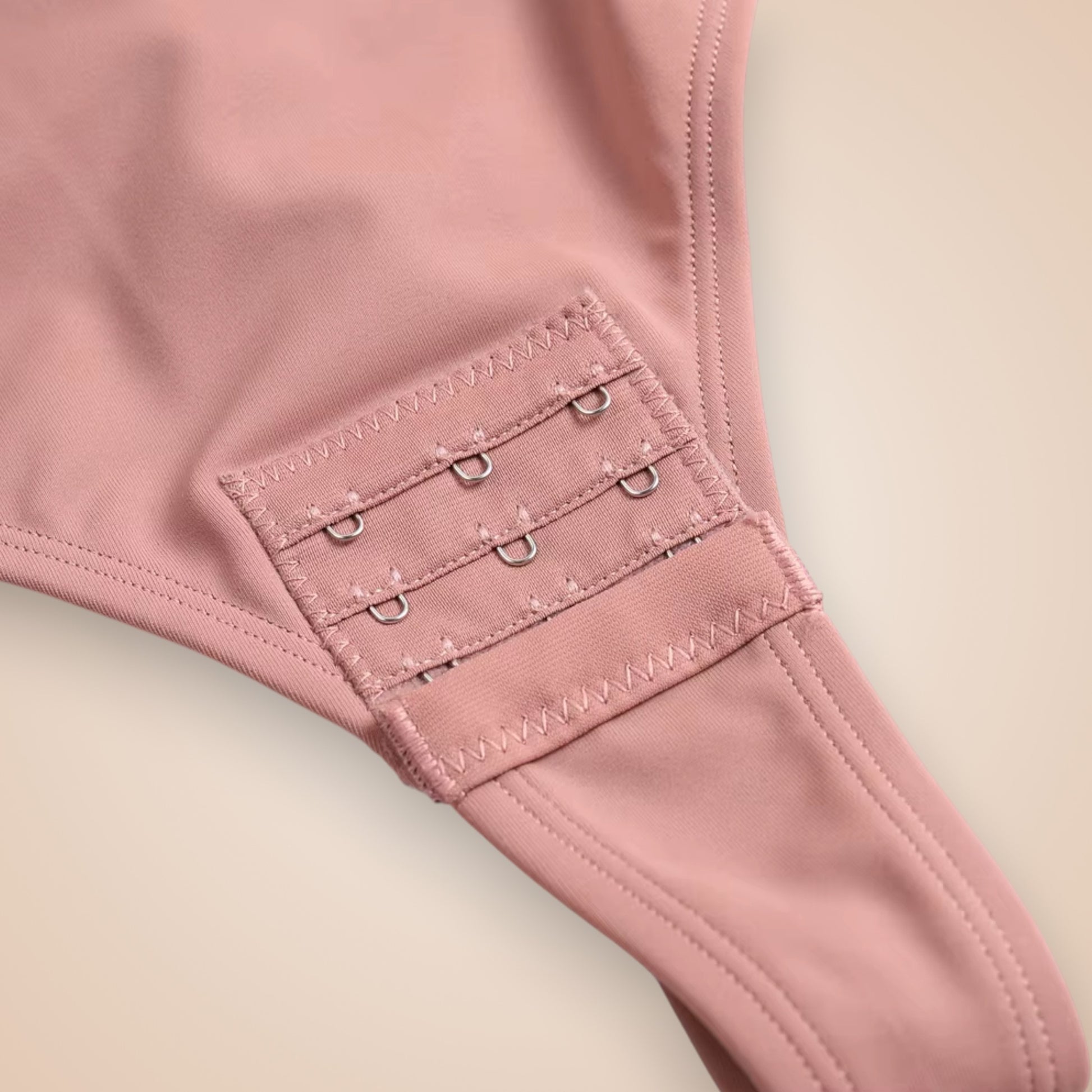 Détail fermeture à crochets sur body gainant sans bretelles rose pâle en tissu lisse.